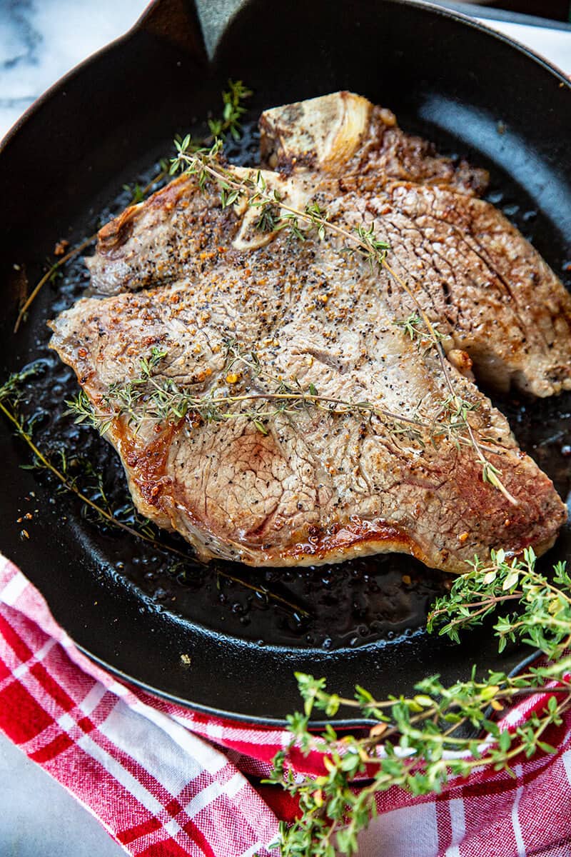 close up Porterhouse Steak in a red skillet with thyme springs on top