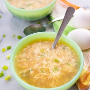 Close up of Egg Drop Soup ready to enjoy! Folded kitchen cloth and 2 fresh eggs on background.