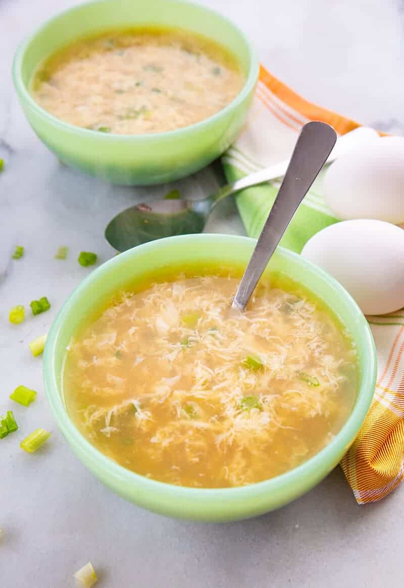 Close up of Egg Drop Soup ready to enjoy! Folded kitchen cloth and 2 fresh eggs on background.