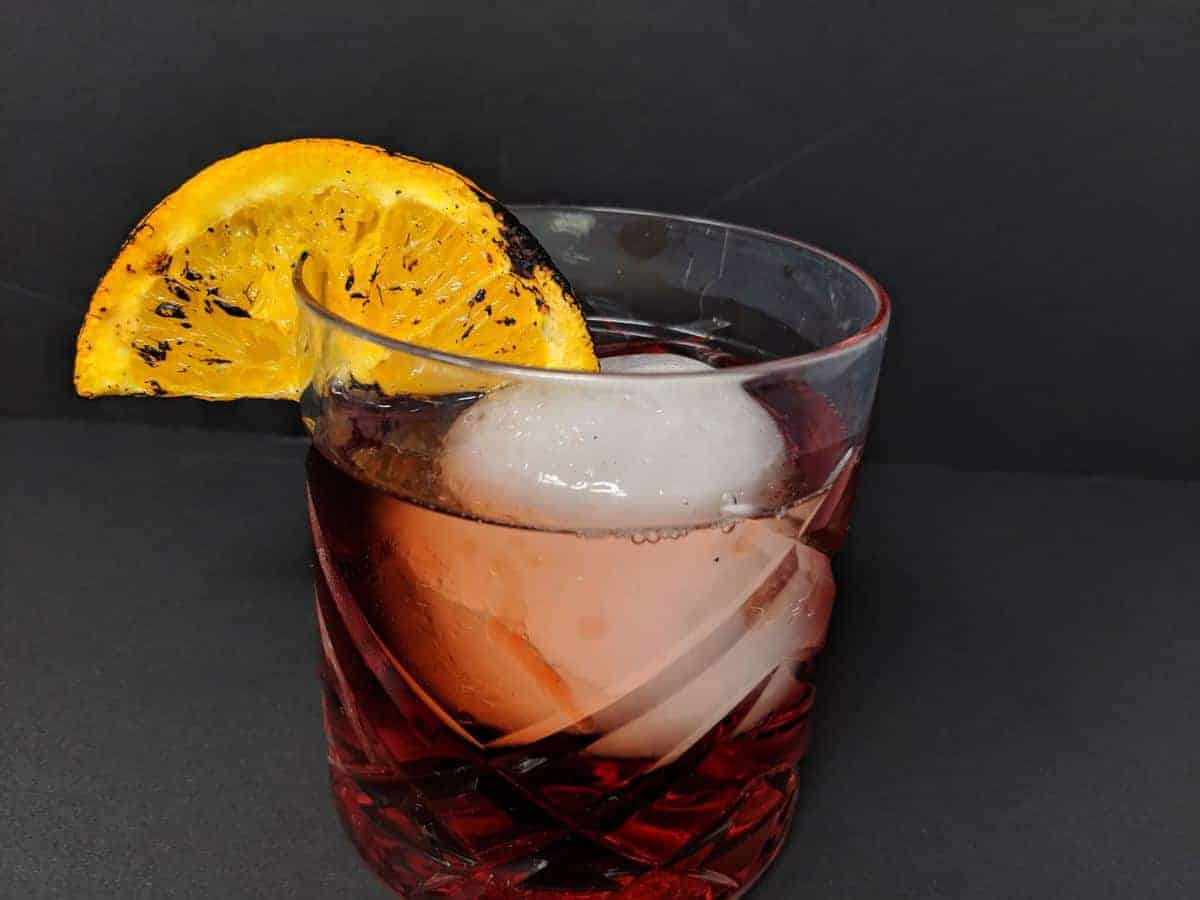 Negroni Cocktail in an old fashioned glass with a large ice cube and a slice of burnt orange 