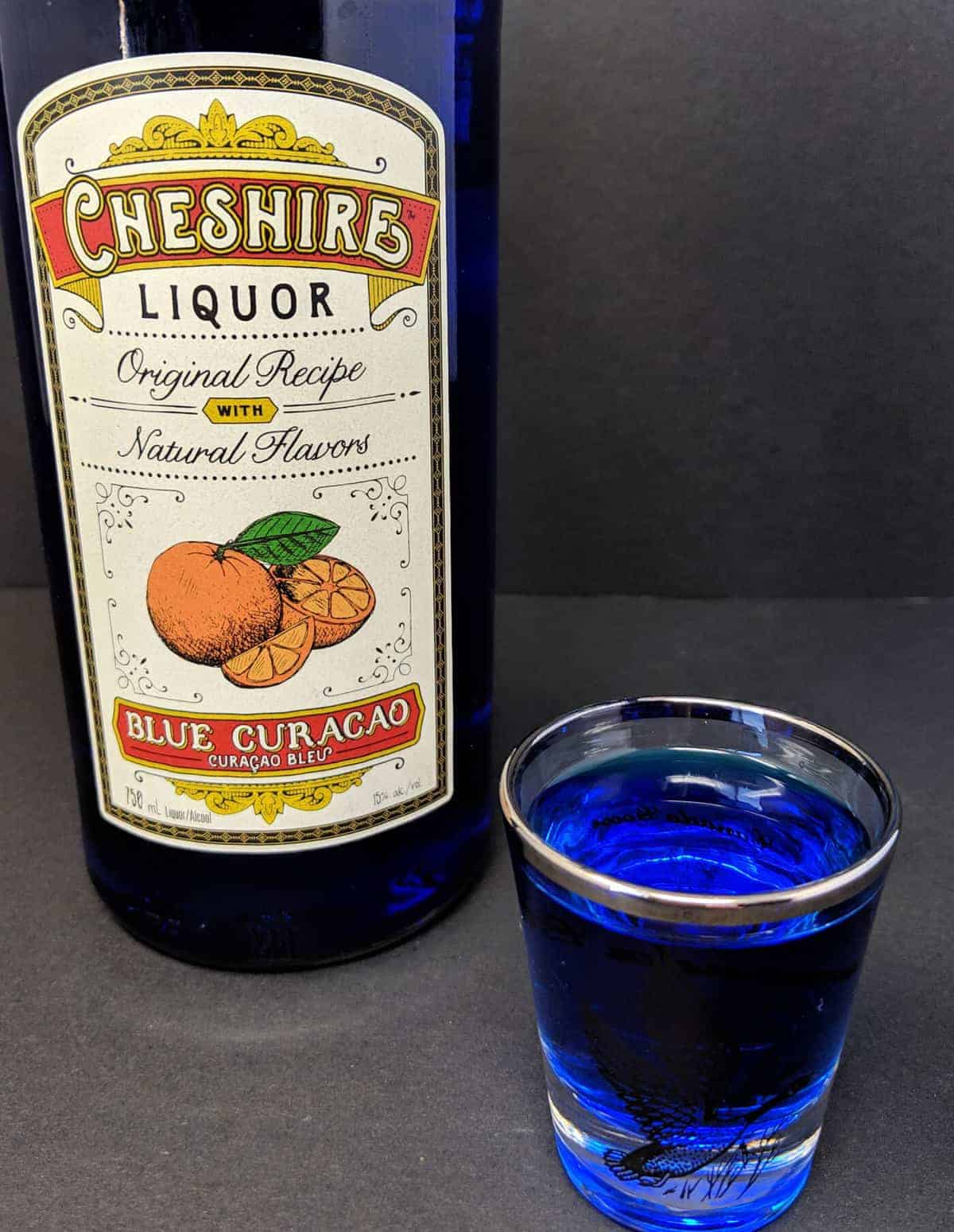 a shot glass with Blue Curaçao and a Bottle of Cheshire Brand Blue Curacao