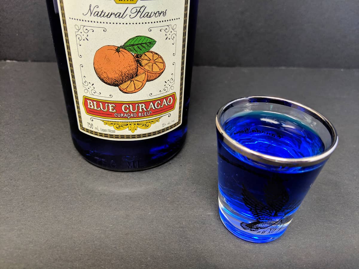 a shot glass with Blue Curaçao and a Bottle of it