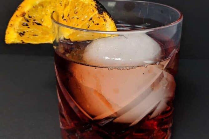 close up Negroni Cocktail in an old fashioned glass with a large ice cube and a slice of burnt orange