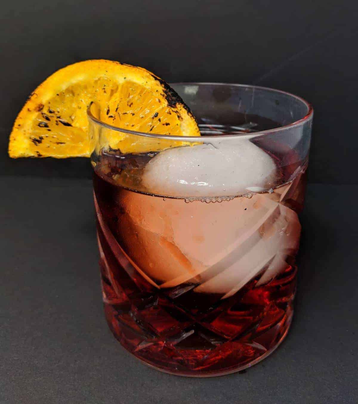 close up Negroni Cocktail in an old fashioned glass with a large ice cube and a slice of burnt orange 