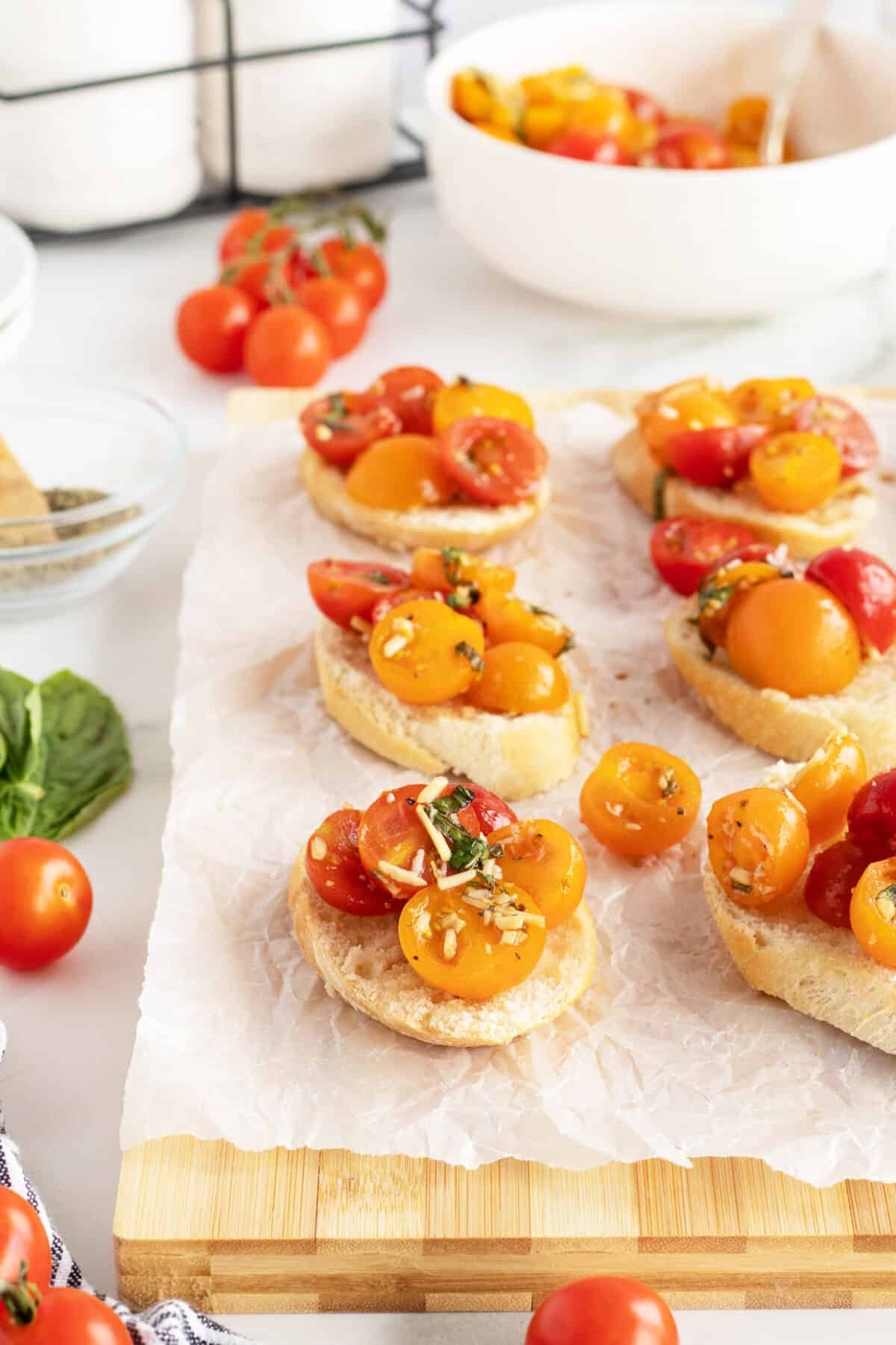Bruschetta on sliced baguetes on a cutting board with parchment paper