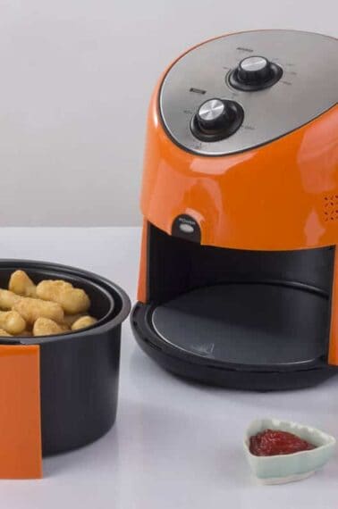 orange color Air fryer machine with chicken and french fries, dipping sauce beside