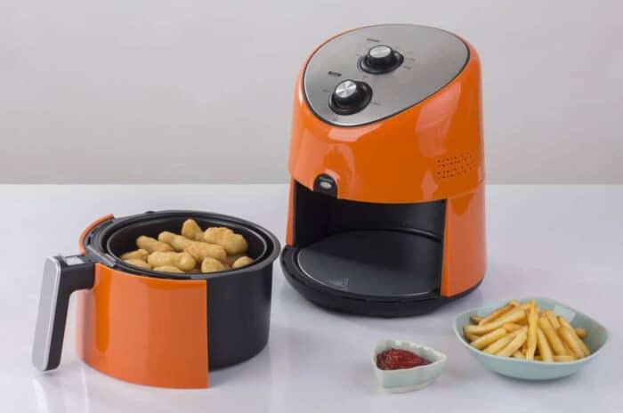 orange color Air fryer machine with chicken and french fries, dipping sauce beside