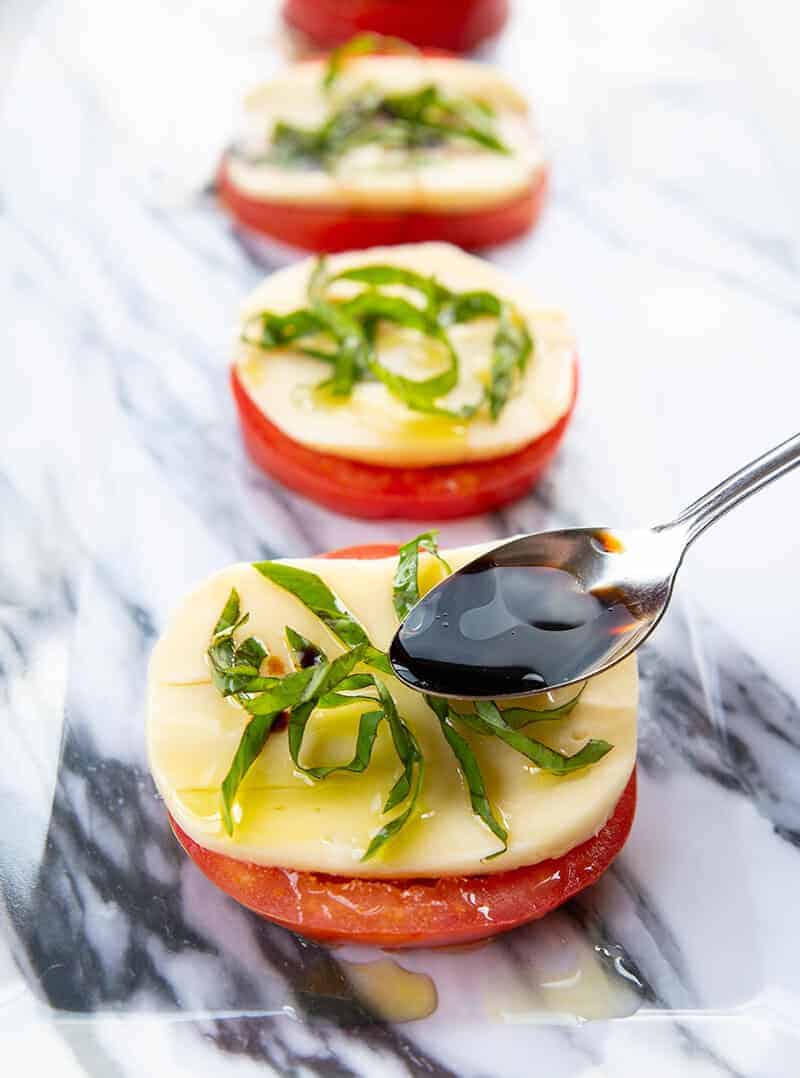 adding some olive oil to a piece of Caprese Salad using a spoon