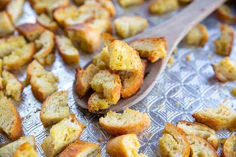 scattered Buttery, Garlicky Homemade Croutons around a wooden spoon