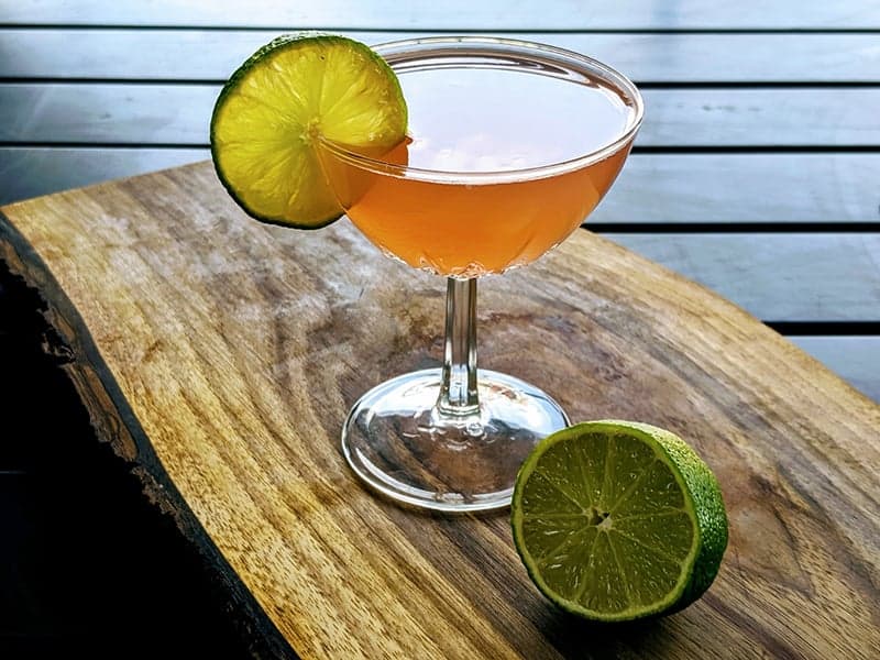 Hemingway Daiquiri in a coupe garnished with lime slice on a wood board with half of a lime.