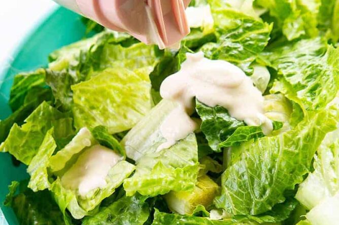 adding the Salad Dressing to a bowl of Caesar salad