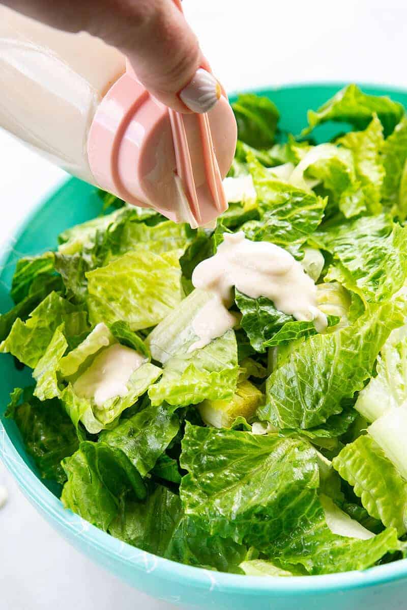 adding the Salad Dressing to a bowl of Caesar salad