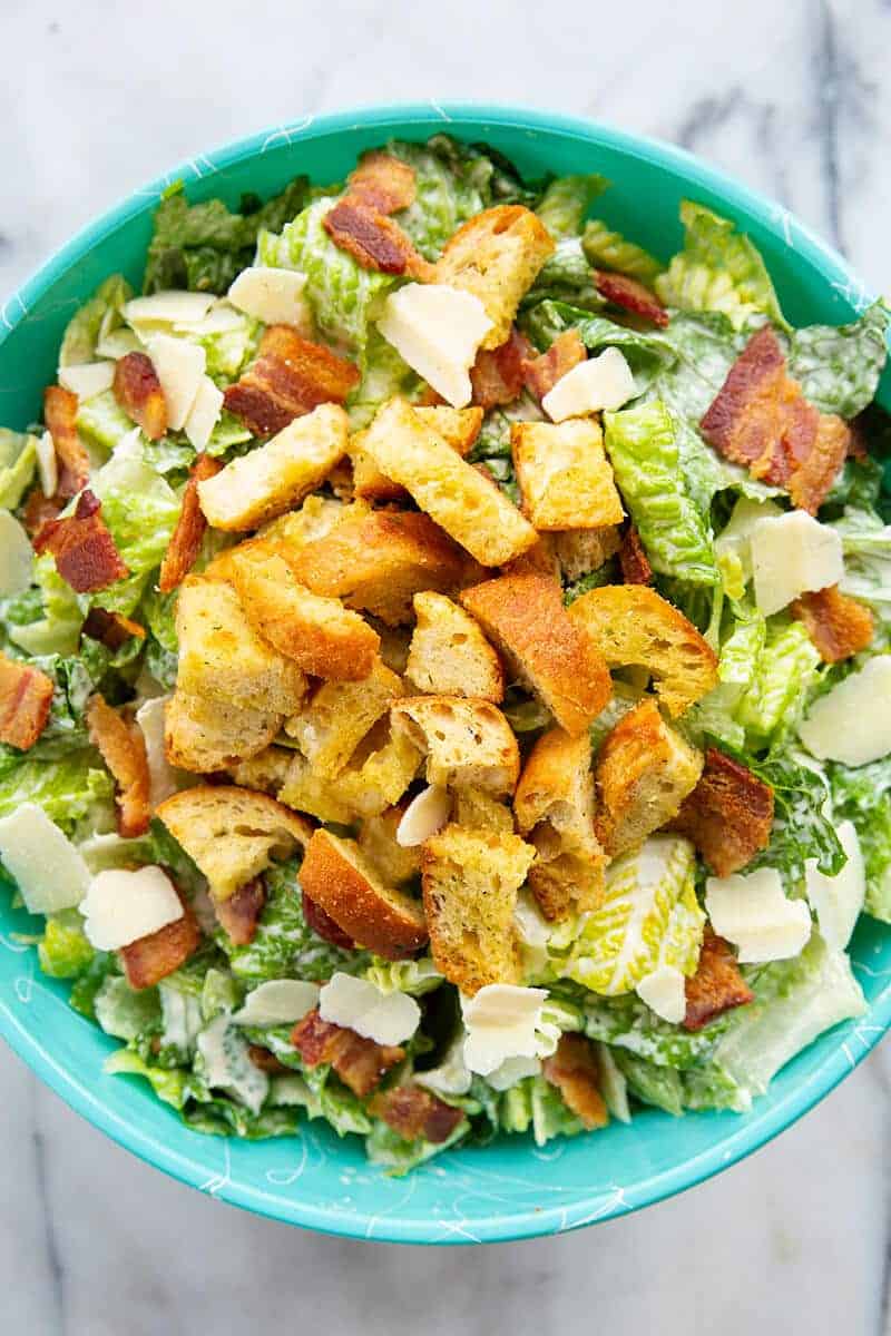 close up Caesar Salad in a jade blue bowl topped with bacon, HOMEMADE CROUTONS and Parmesan