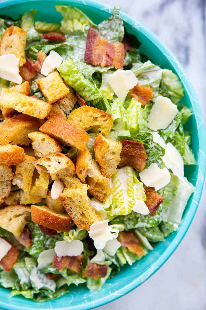 close up Caesar Salad in a jade blue bowl topped with bacon, HOMEMADE CROUTONS and Parmesan