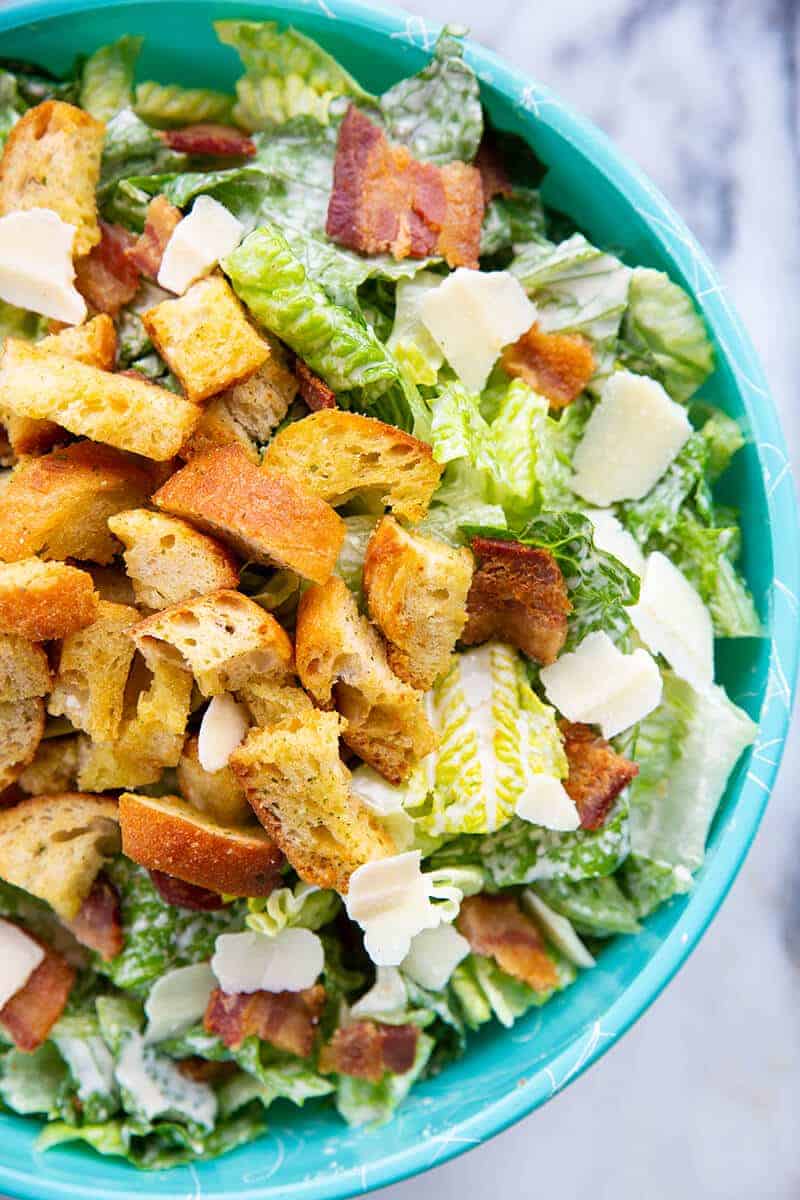 close up Caesar Salad in a jade blue bowl topped with bacon, HOMEMADE CROUTONS and Parmesan