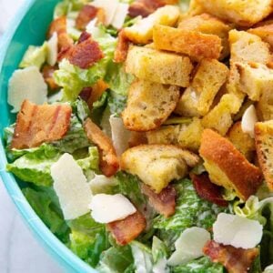 Caesar Salad in a jade blue bowl topped with bacon, HOMEMADE CROUTONS and Parmesan