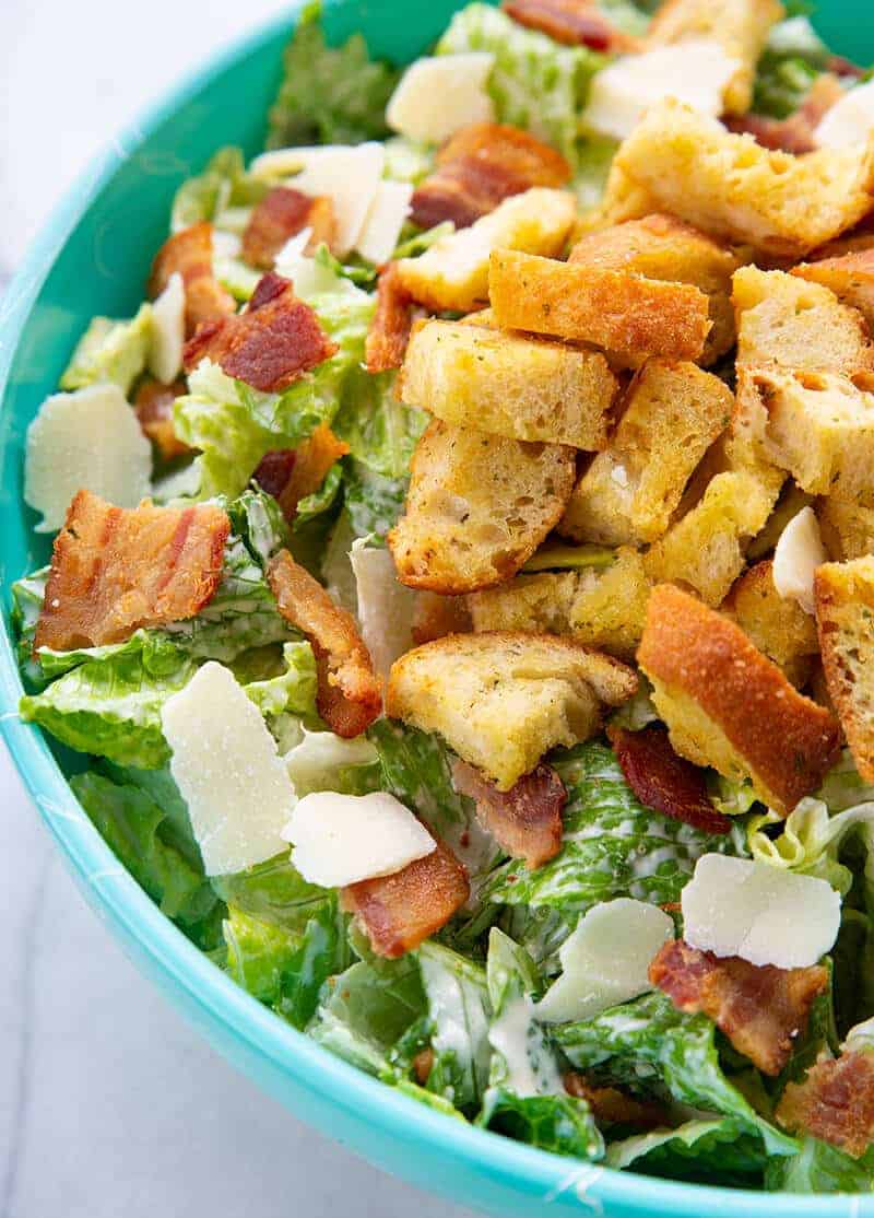 Caesar Salad in a jade blue bowl topped with the bacon, HOMEMADE CROUTONS and Parmesan