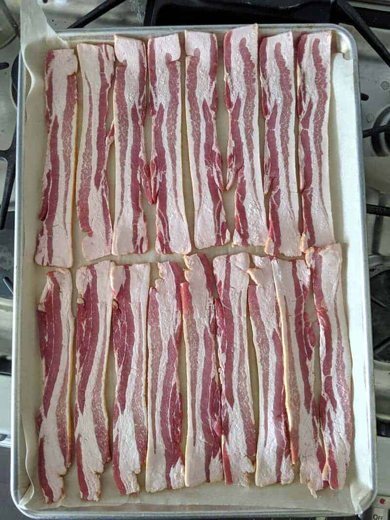 uncooked bacon placed on a baking sheet