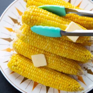 getting a piece of hot buttered corn on the cob on a plate using kitchen tongs