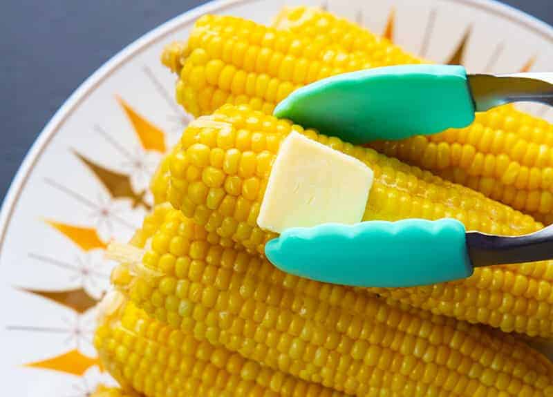getting a piece of Instant Pot Corn on the Cob with a slice of butter using kitchen tongs