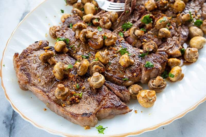 New York Strip Steak with Fried Garlic Mushrooms in a white plate