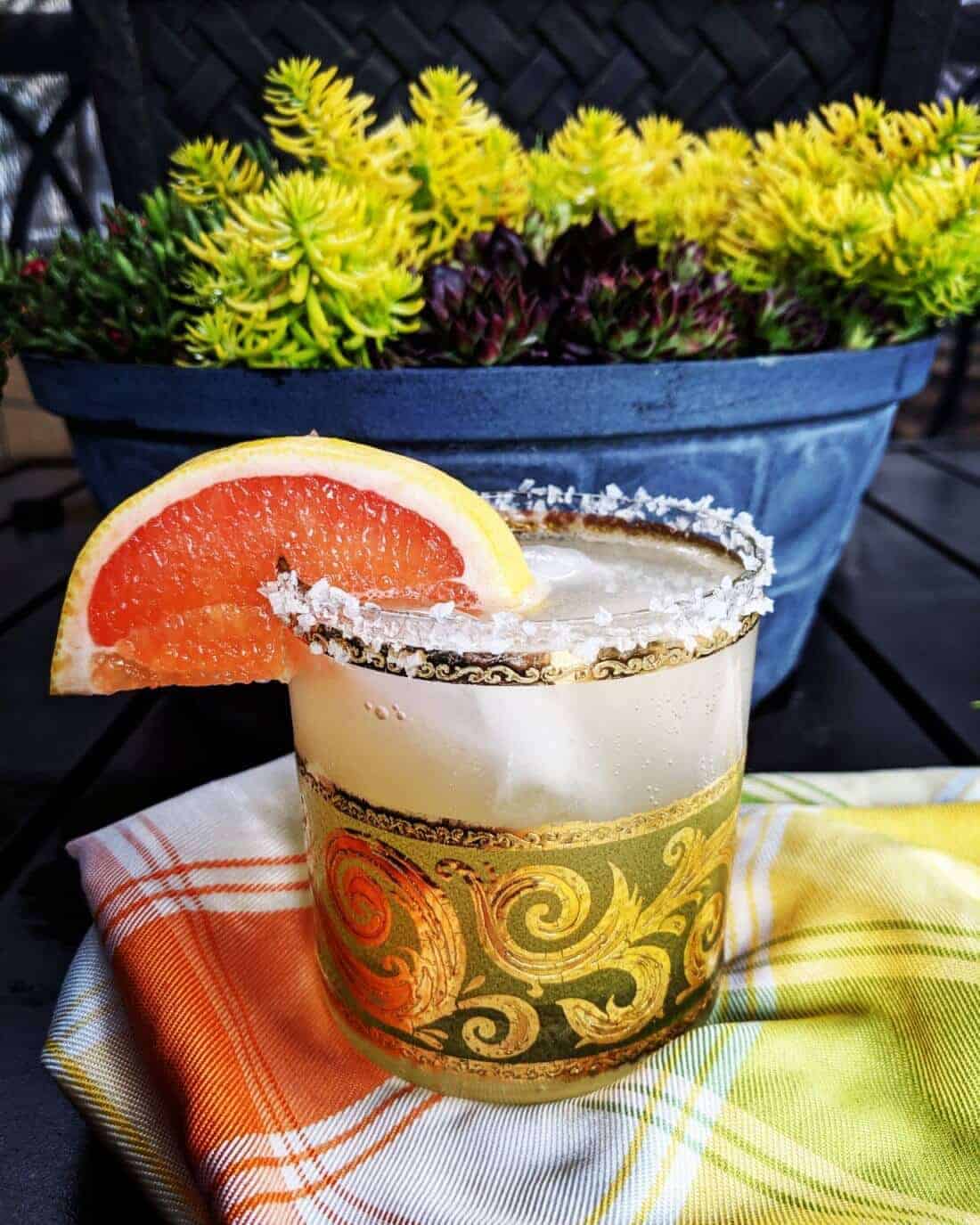 checkered tablecloth underneath a glass of Paloma Cocktail with Salted Rim garnish with a slice of grapefruit