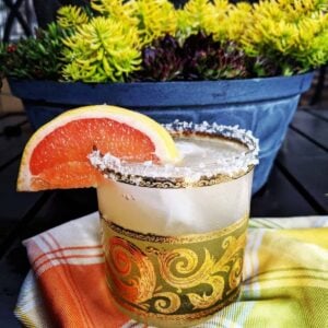 checkered tablecloth underneath a glass of Paloma Cocktail with Salted Rim garnish with a slice of grapefruit