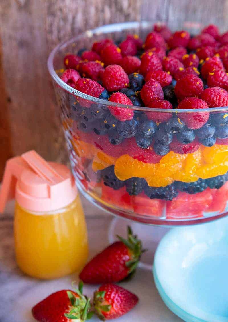 Fruit salad, container of orange juice dressing and blue Pyrex plates