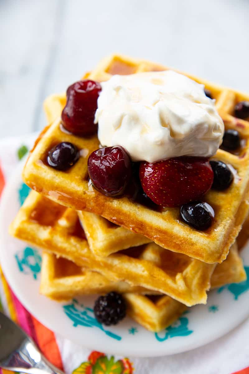 close up stack of Homemade Belgian Waffles topped with some berries and Whipped Cream