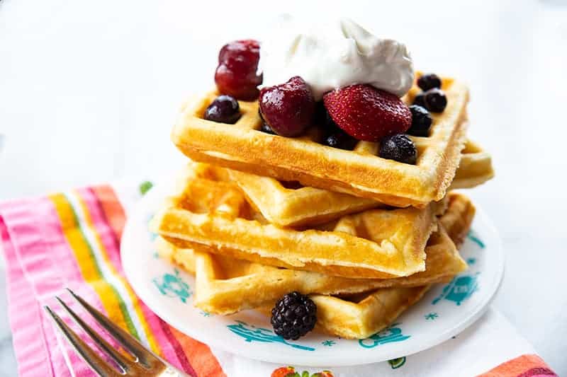 a plate with a stack of Homemade Belgian Waffles topped with some berries and Whipped Cream