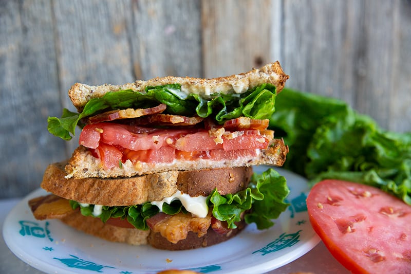 Classic BLT Sandwich in a white plate, some lettuce and a slice of tomato in background