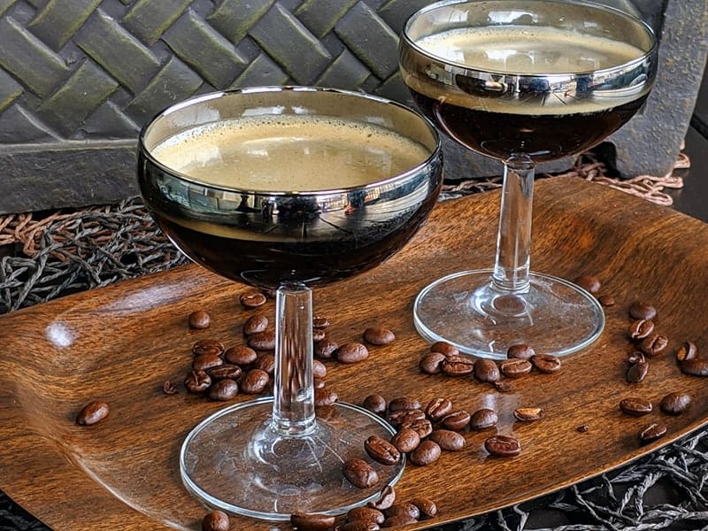 close up Two coupes on a wood serving tray with coffee beans scattered upon it.