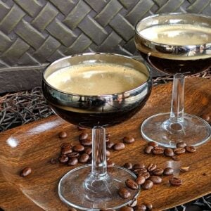 close up Two coupes on a wood serving tray with coffee beans scattered upon it.