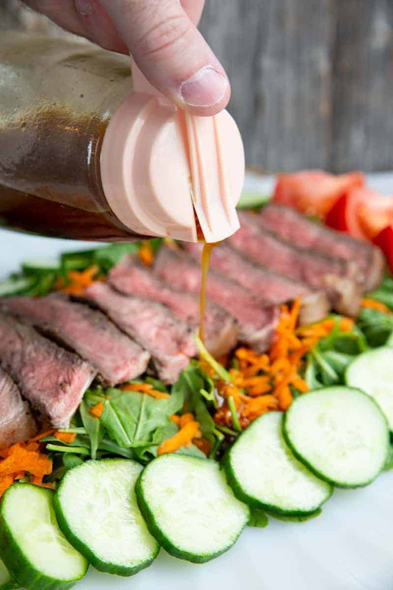 Asian Sesame Grilled Steak Salad in a white serving plate, drizzled with salad dressing