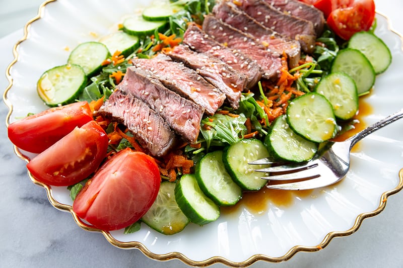 Asian Sesame Grilled Steak Salad in a white serving plate, drizzled with salad dressing and sprinkled with sesame seeds