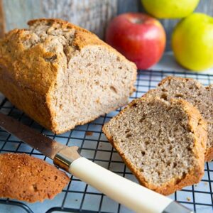 close up bread knife and sliced Cinnamon Spice Apple Bread in a wire rack, apples on background