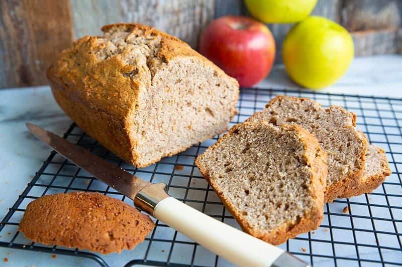 bread knife and sliced Cinnamon Spice Apple Bread in a wire rack, apples on background