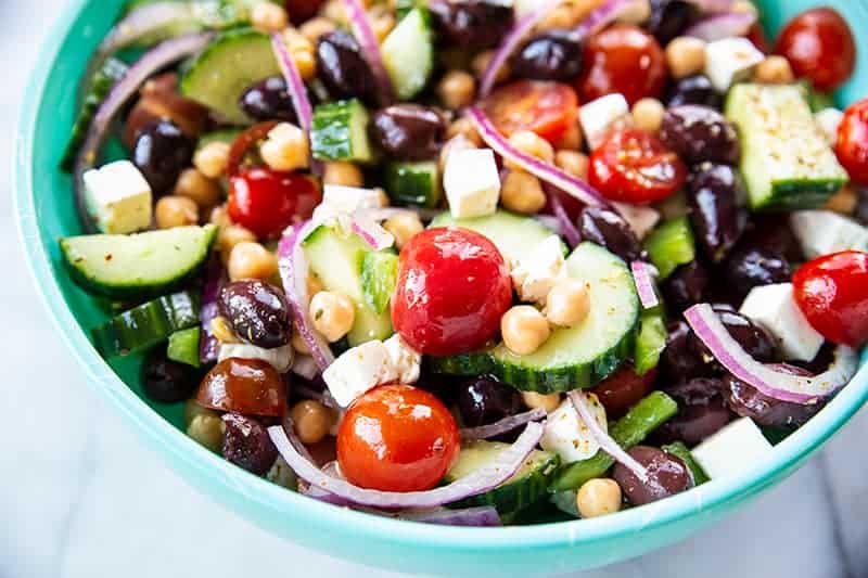 Mediterranean Chickpea Salad in a blue serving bowl with a drizzle of olive oil and a sprinkle of Greek seasoning