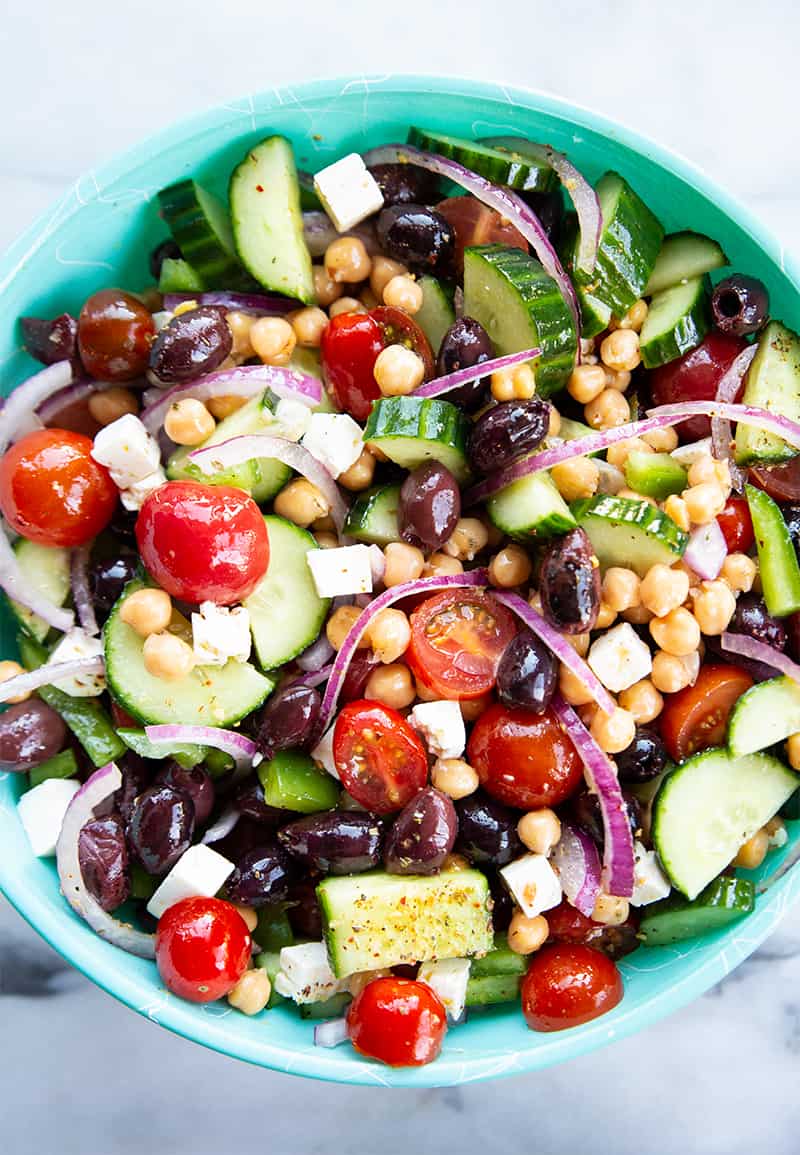 close up Mediterranean Chickpea Salad in a blue serving bowl with a drizzle of olive oil and a sprinkle of Greek seasoning