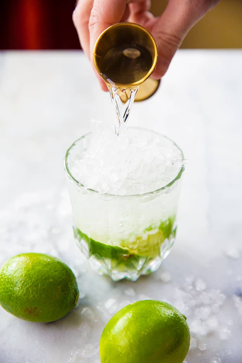 Pouring Cachaça from a shot glass into a cocktail glass for a Caipirinha