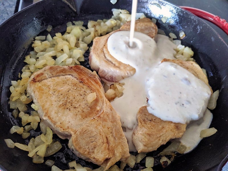 pouring mushroom sauce onto browned pork chops in a skillet 