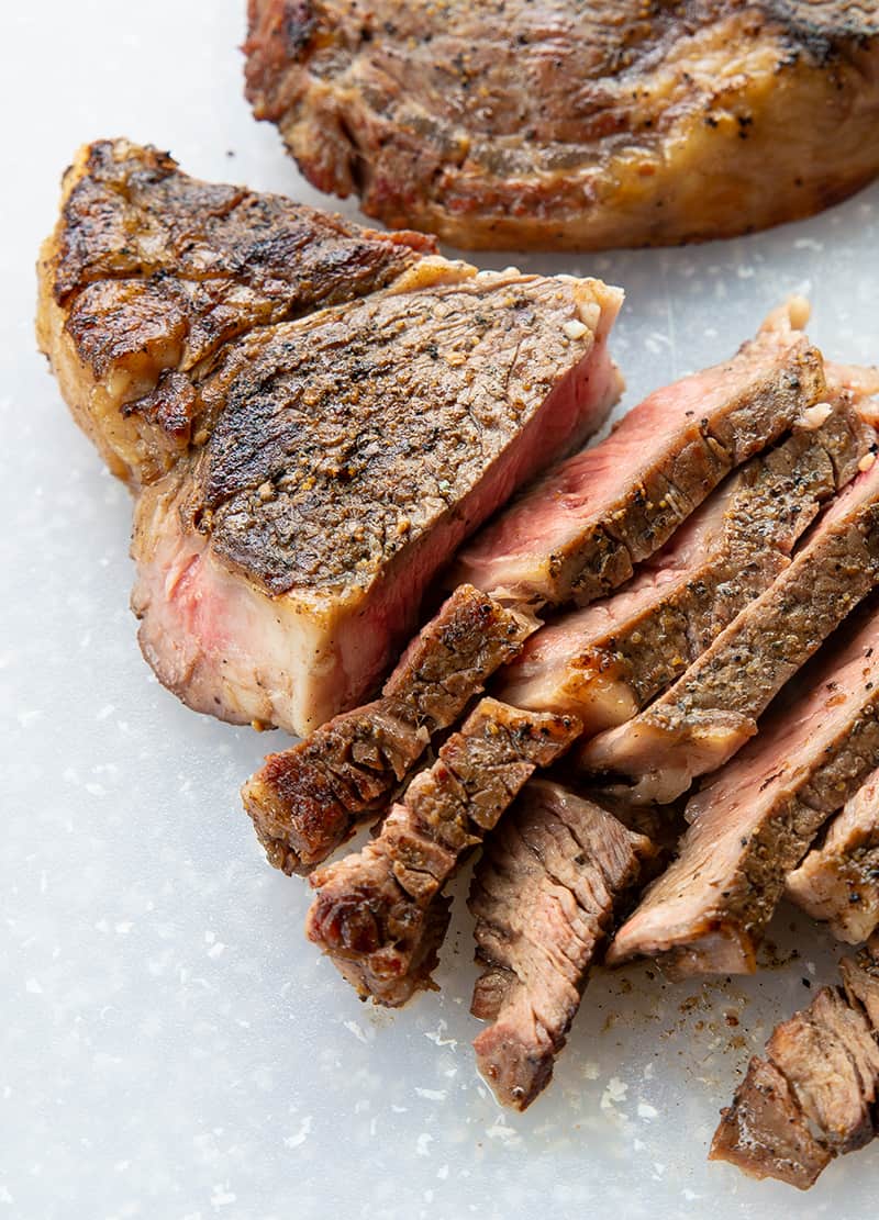 close up of medium-rare rib eye steak sliced on a white cutting board