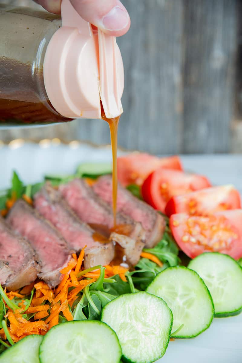 close up pouring Homemade Asian Salad Dressing to steak salad