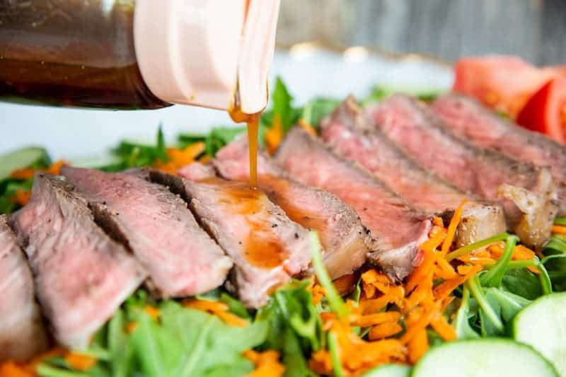 pouring Homemade Asian Salad Dressing to steak salad