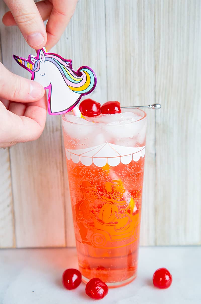 close up adding unicorn straw to Shirley Temple drink, garnish with maraschino cherries