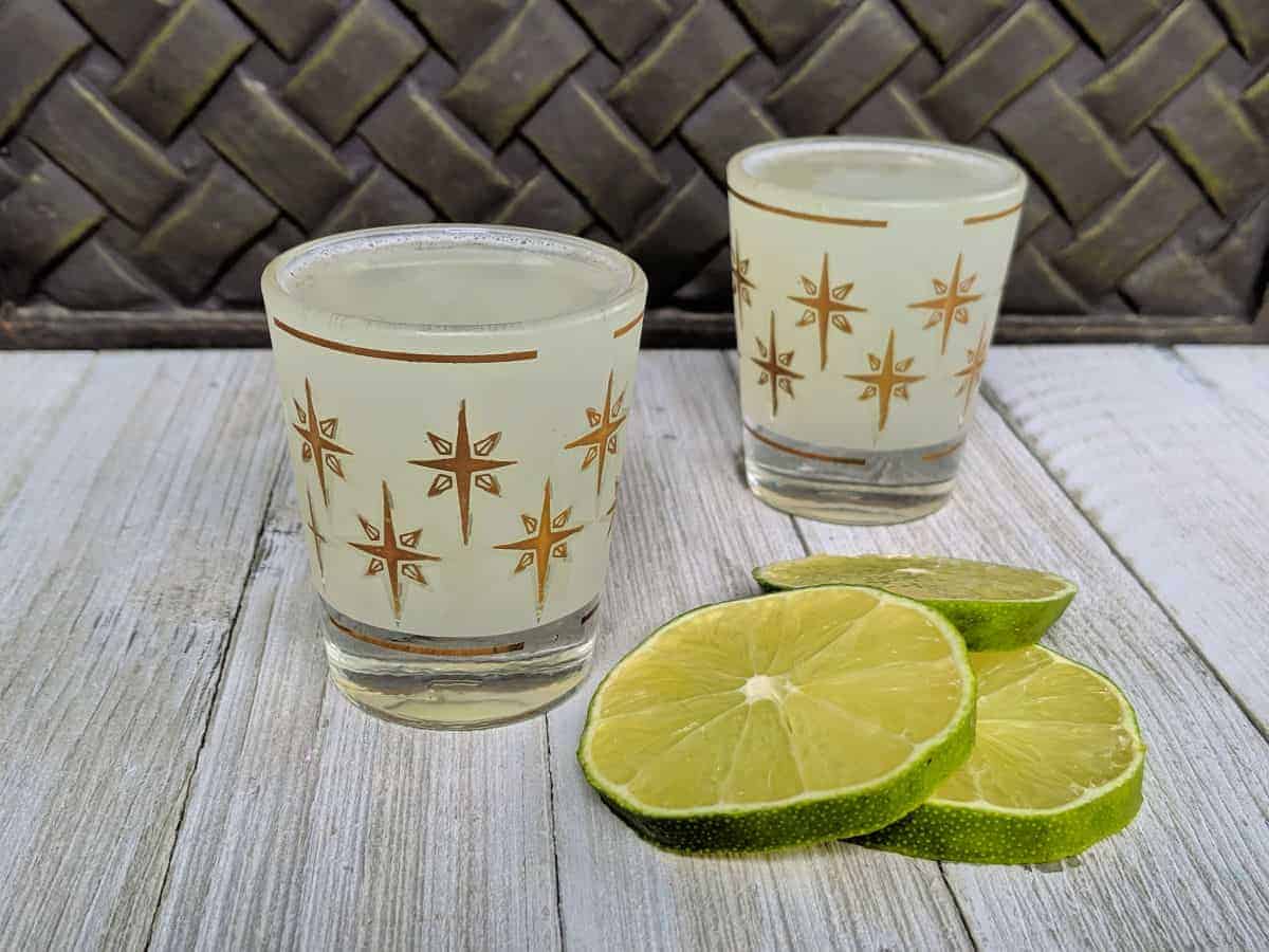 two shot glasses with kamikaze cocktail on a board with lime slices
