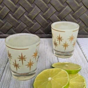 Two shot glasses with alcohol on a board with lime slices