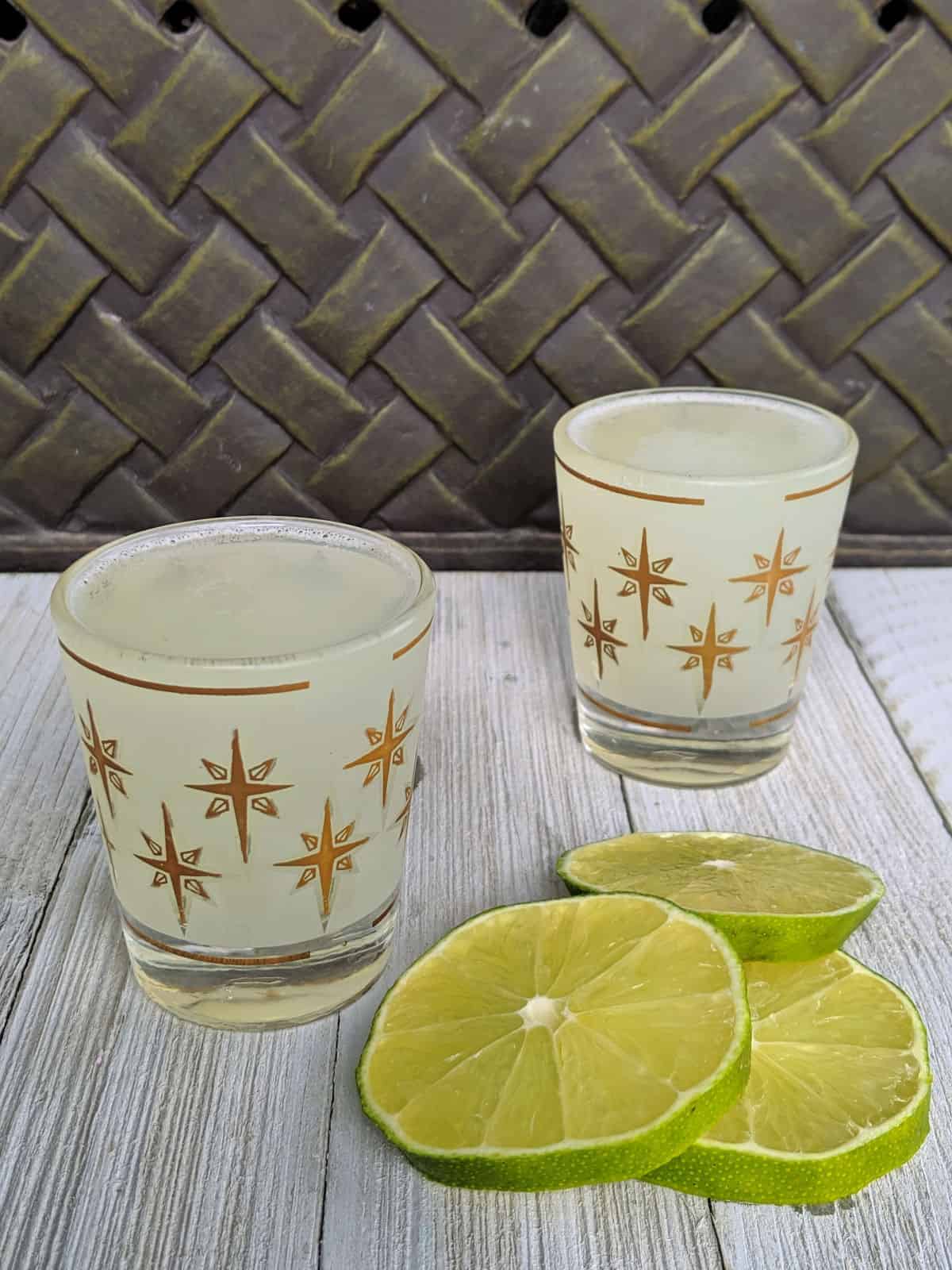 Two shot glasses with alcohol on a board with lime slices