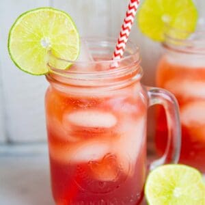 close up Madras Vodka Drink with red white straws on mason jars with handle, garnish with lime slices