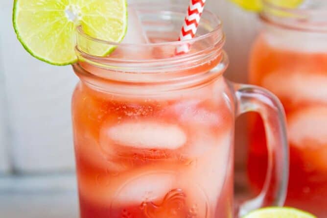 close up Madras Vodka Drink with red white straws on mason jars with handle, garnish with lime slices